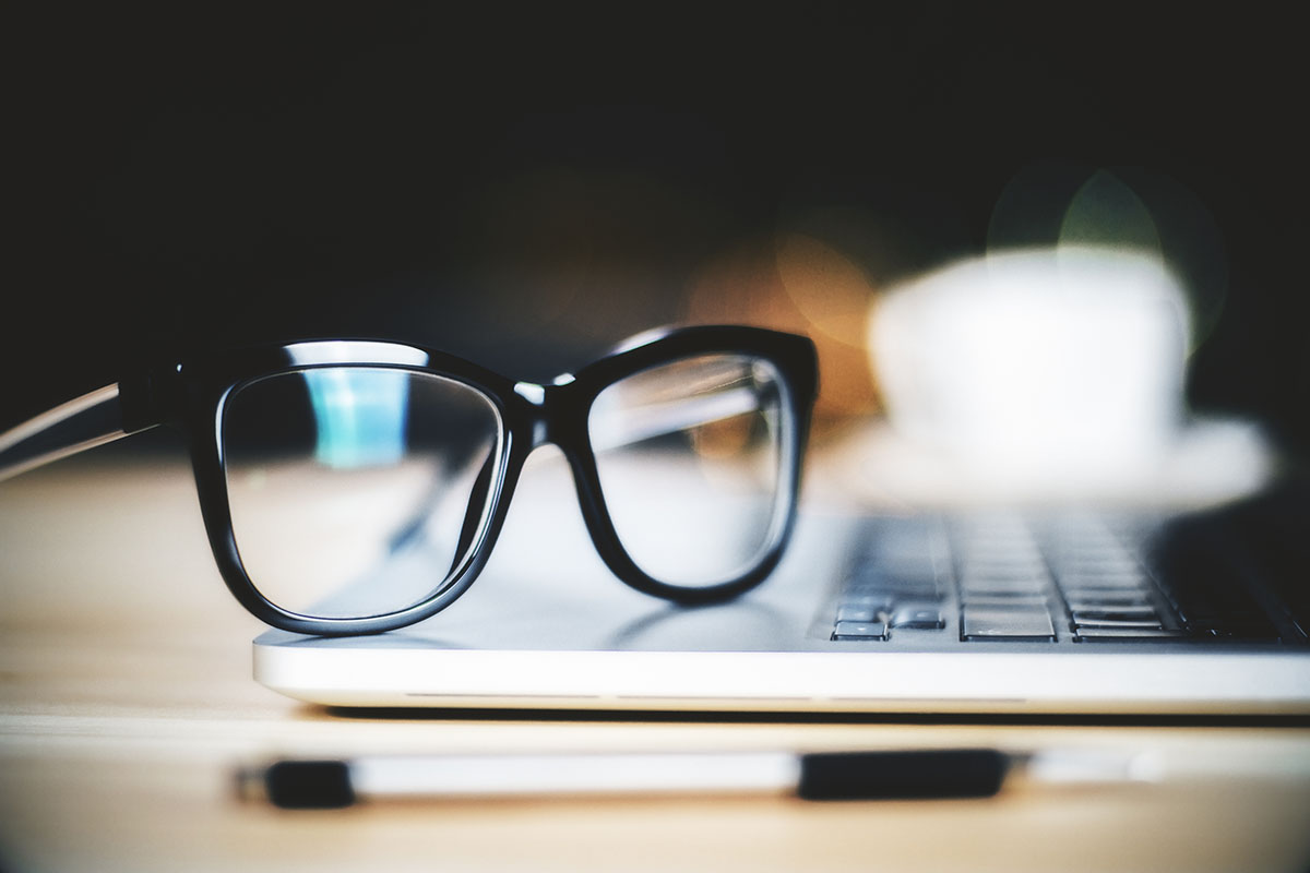 Glasses on laptop with pen, close up